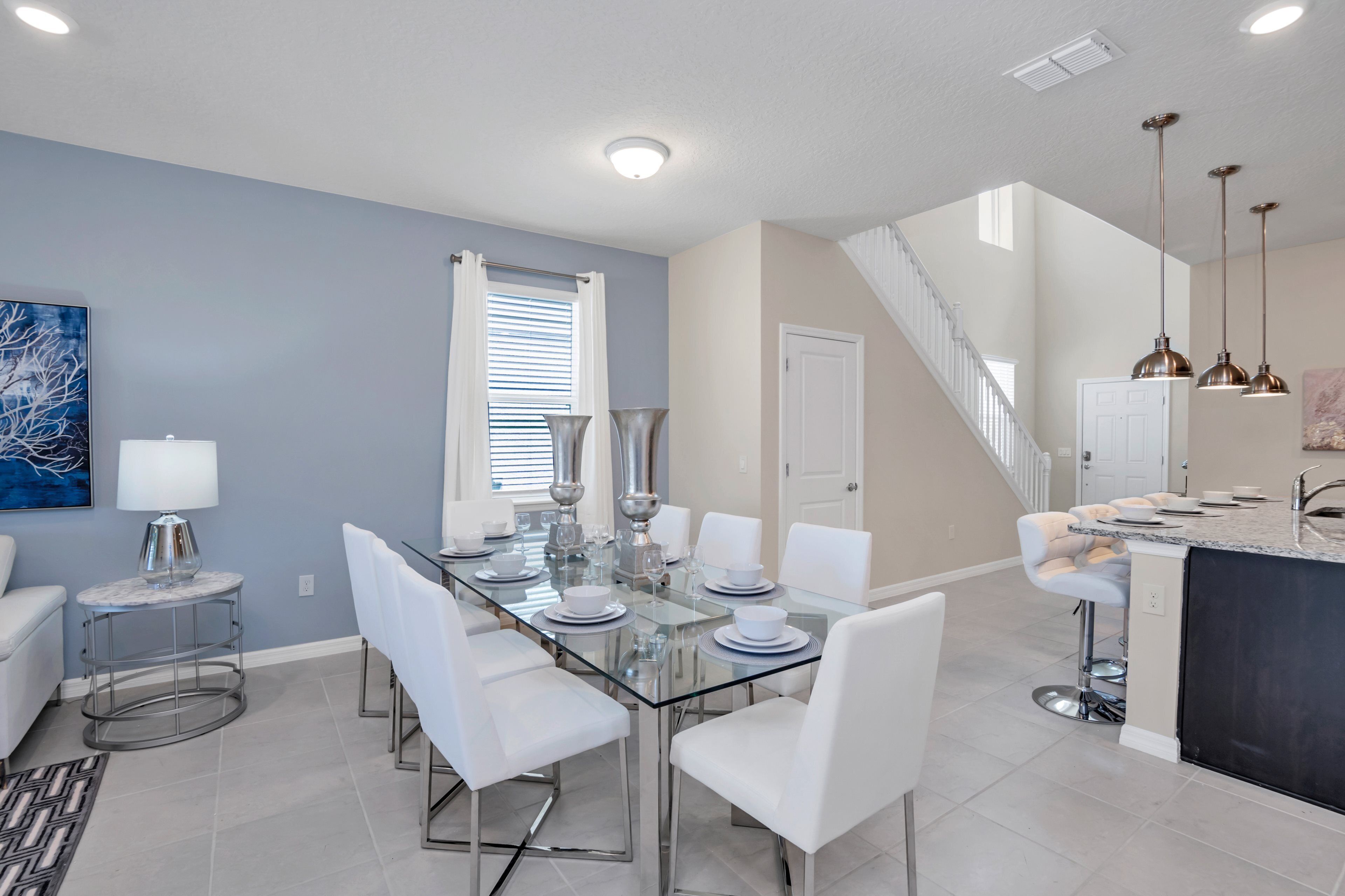 A modern kitchen with a central island, a dining area with a glass table, and a staircase leading to an upper level.