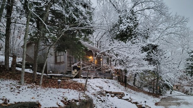A rustic cabin with a wooden exterior, surrounded by snow-covered trees and a stone pathway leading to the entrance. - Cowboy Cabin, come sit under the trees (Marthasville)