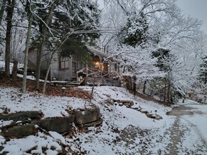 A rustic cabin with a wooden exterior, surrounded by snow-covered trees and a stone pathway leading to the entrance. - Cowboy Cabin, come sit under the trees (Marthasville)