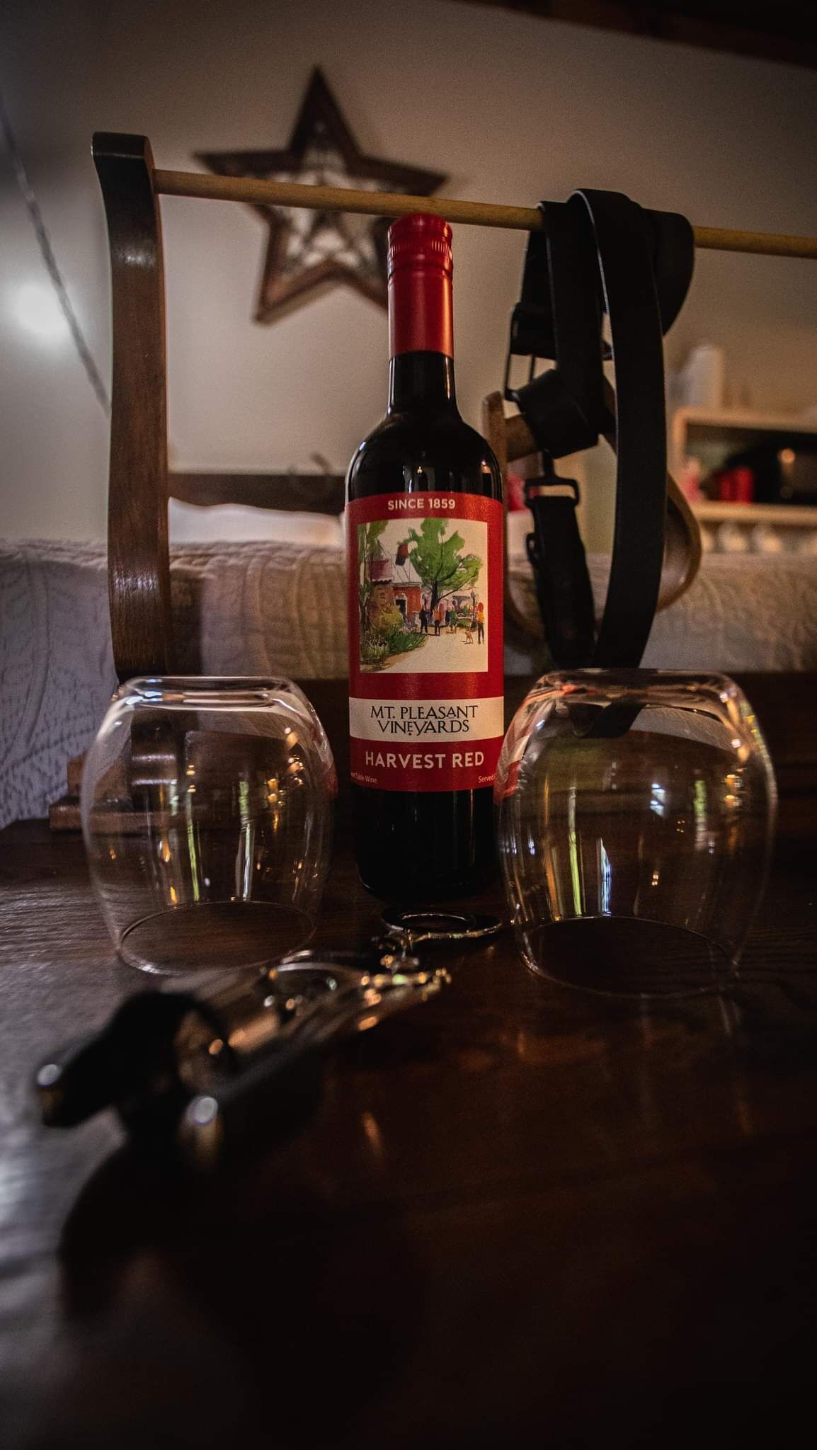 A bottle of wine with a label, two empty glasses, and a bottle opener on a wooden surface.