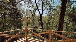 A wooden deck with a simple railing, surrounded by dense forest. - Cowboy Cabin, come sit under the trees (Marthasville)