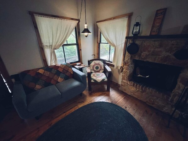A cozy room with a fireplace, a sofa, a chair, and a small table. - Cowboy Cabin, come sit under the trees (Marthasville)