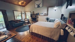 A cozy room with a large bed, a fireplace, a sofa, and a dining table set for two. - Cowboy Cabin, come sit under the trees (Marthasville)