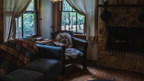 A cozy living room with a wooden ceiling, a fireplace, a sofa, and a chair. - Cowboy Cabin, come sit under the trees (Marthasville)