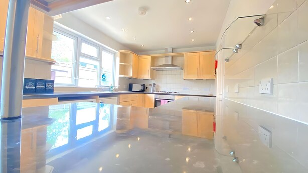 A modern kitchen with wooden cabinets, a stainless steel range hood, and a large window providing natural light. - Airport Comfy Stay (West Drayton)