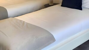 A hotel room with two beds, each with white bedding and black pillows, and a small table with a lamp between them. - Airport Comfy Stay (West Drayton)