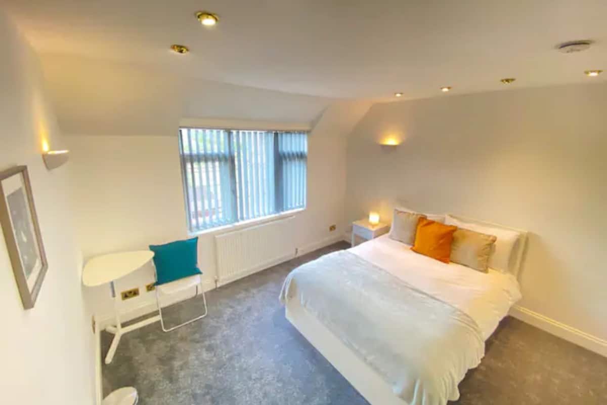 A bedroom with a bed, a small desk, and a window.