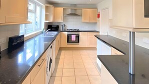 A modern kitchen with light-colored cabinets, a black countertop, and a stainless steel range hood. - Airport Comfy Stay (West Drayton)