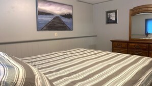 Une chambre à coucher avec un lit, une commode, un tableau représentant une jetée et un tableau encadré accroché au mur.