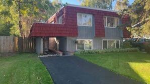 Une maison à deux étages, avec un toit recouvert de bardeaux rouges, un porche à l’avant et une allée pavée.