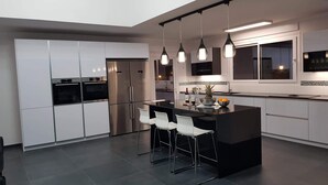 Une cuisine moderne avec des meubles blancs, des appareils en acier inoxydable et un îlot central doté de tabourets de bar.