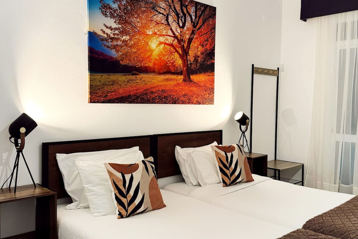Ein Schlafzimmer mit einem großen Bett, zwei Nachttischen, einem Schminktisch, einem Spiegel und einem Baumgemälde.