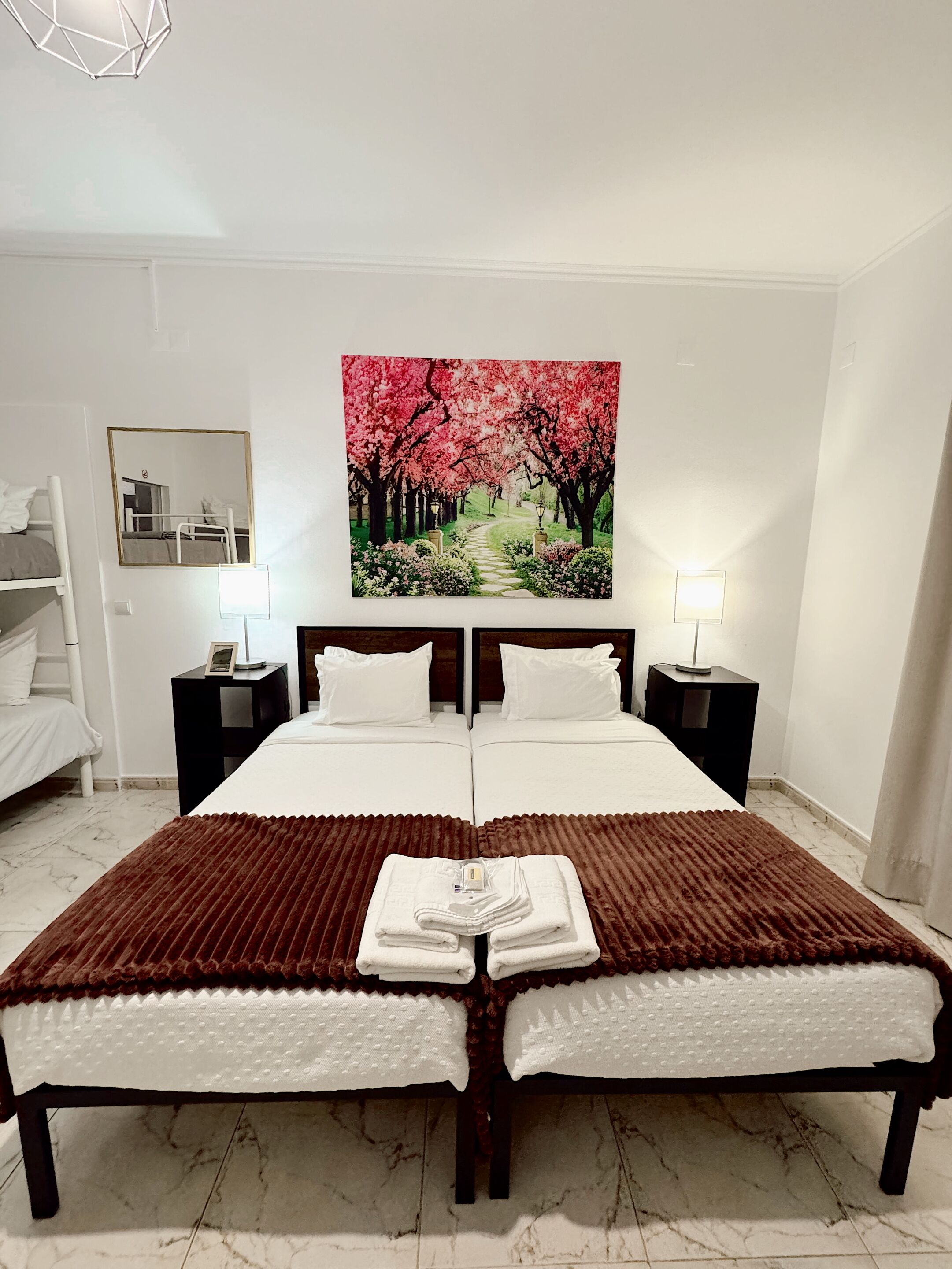 Una habitación de hotel con una cama grande, dos mesitas de noche con lámparas, un cuadro de un sendero de cerezos y un armario blanco.