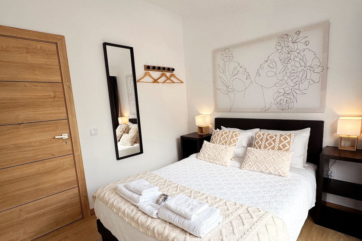 Ein Schlafzimmer mit einem Holzschrank, einem Bett mit weißer Bettwäsche, einem Spiegel, einem Wandbild und Nachttischlampen.