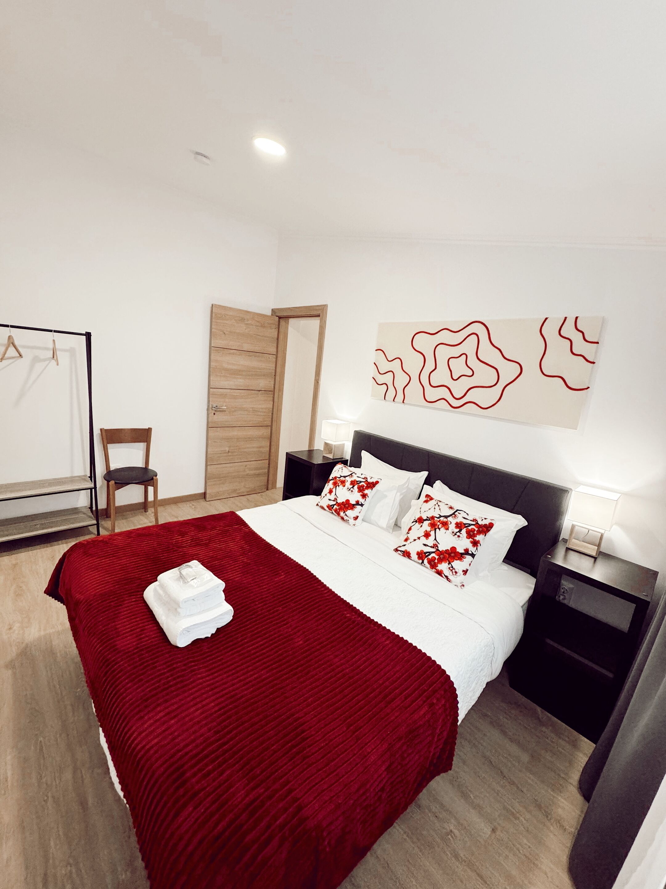 A neatly arranged hotel room with a large bed, a wooden door, a chair, and a wall-mounted artwork.