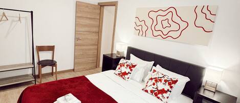 A neatly arranged hotel room with a large bed, a wooden door, a chair, and a wall-mounted artwork.