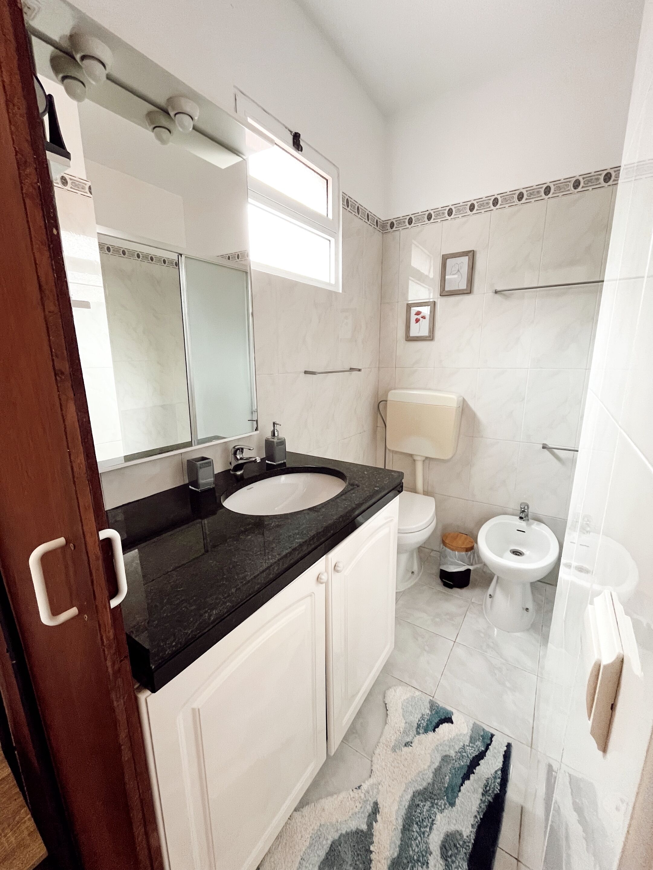 Een badkamer met een wit wastafel, een spiegel, een toilet en een bidet.