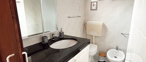 A bathroom with a white sink, a mirror, a toilet, and a bidet.