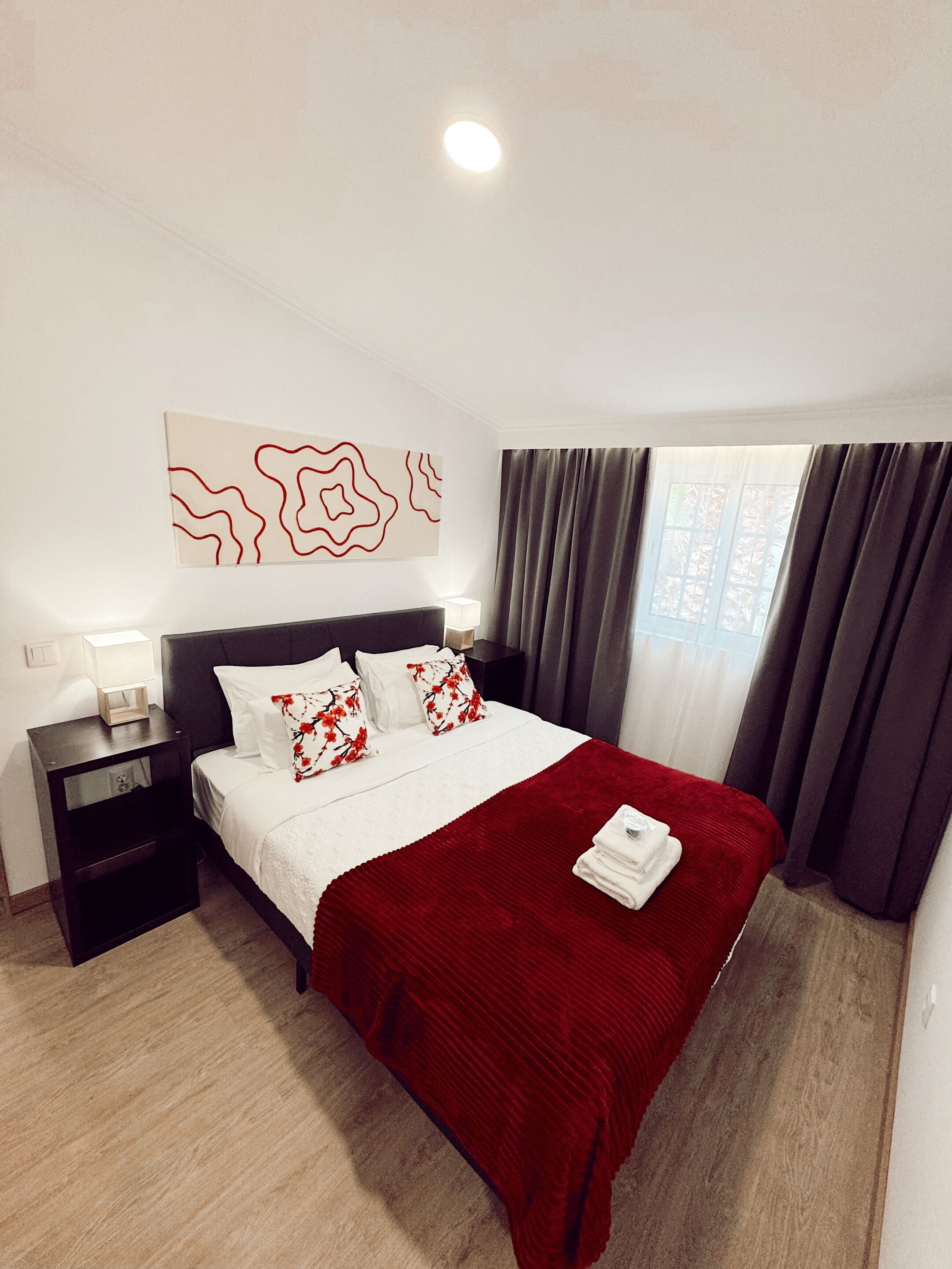 A hotel room with a bed, a nightstand, a wall art piece, and a window with curtains.