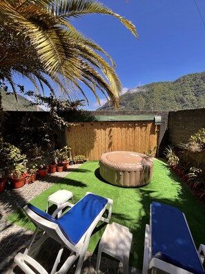 Ein Garten mit Kunstgrasanlage, Whirlpool, Liegestühlen und Topfpflanzen.