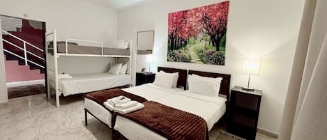 Habitación de hotel con literas, una cama individual, un cuadro de un sendero de cerezos, una lámpara de noche y un espejo en la pared.