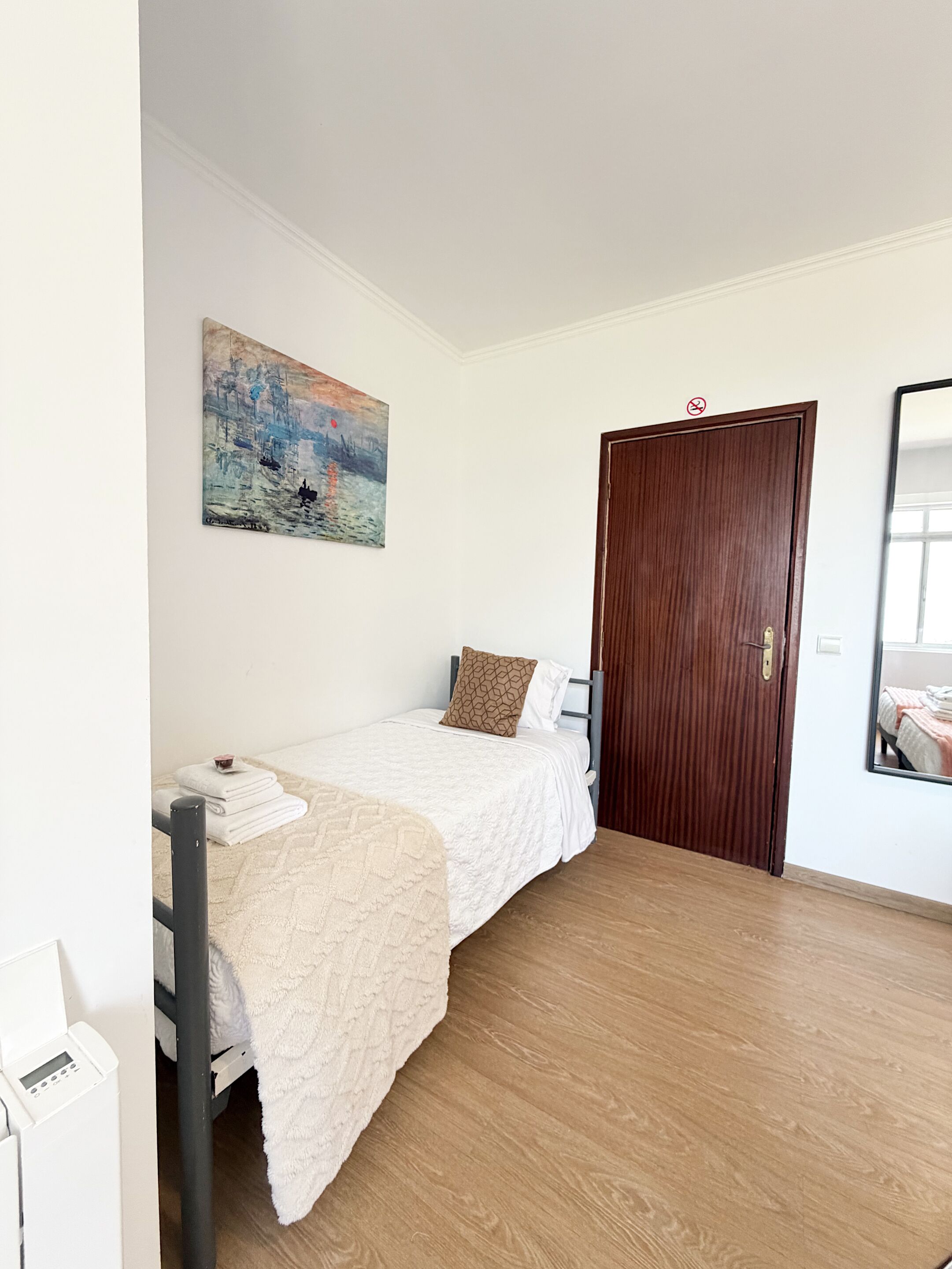 A bedroom with a bed, a painting, a wooden door, and a mirror.