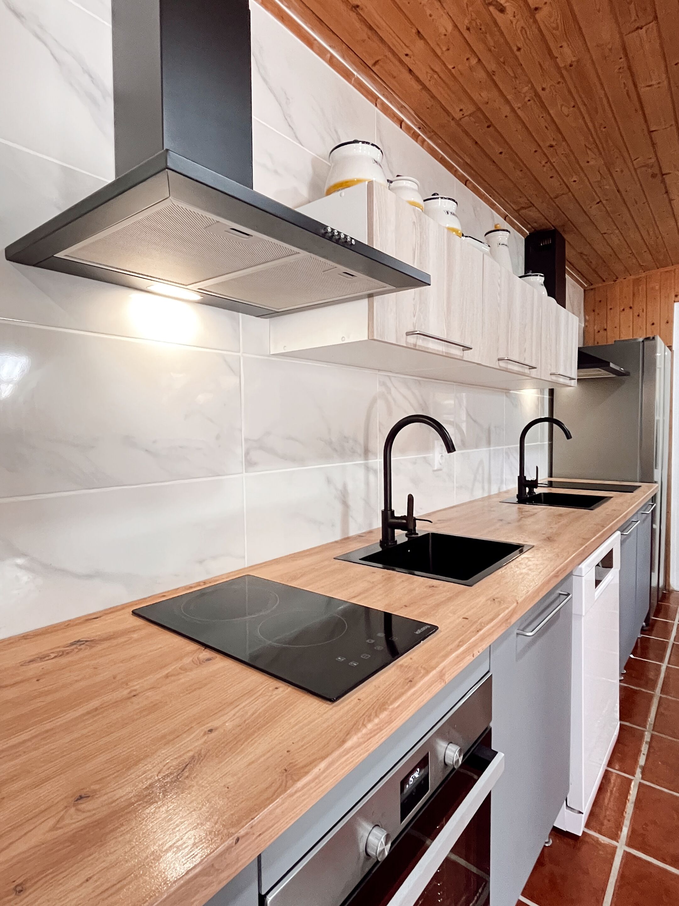 Una cocina moderna con encimera de madera, dos lavabos negros, una campana extractora de acero inoxidable y un horno empotrado.