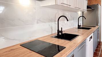 Una cocina moderna con encimera de madera, dos lavabos negros, una campana extractora de acero inoxidable y un horno empotrado.