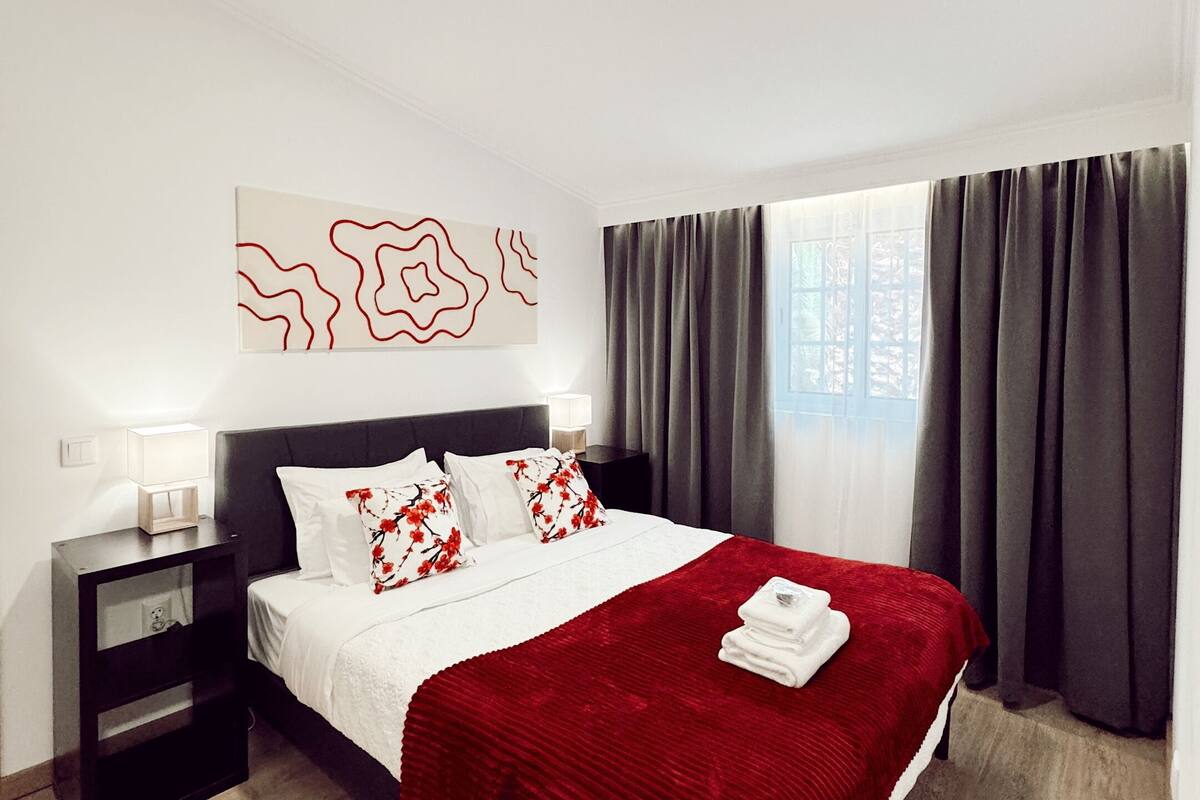 Ein Hotelzimmer mit einem Bett, einem Nachttisch, einem Kunstwerk an der Wand und einem Fenster mit Vorhängen.