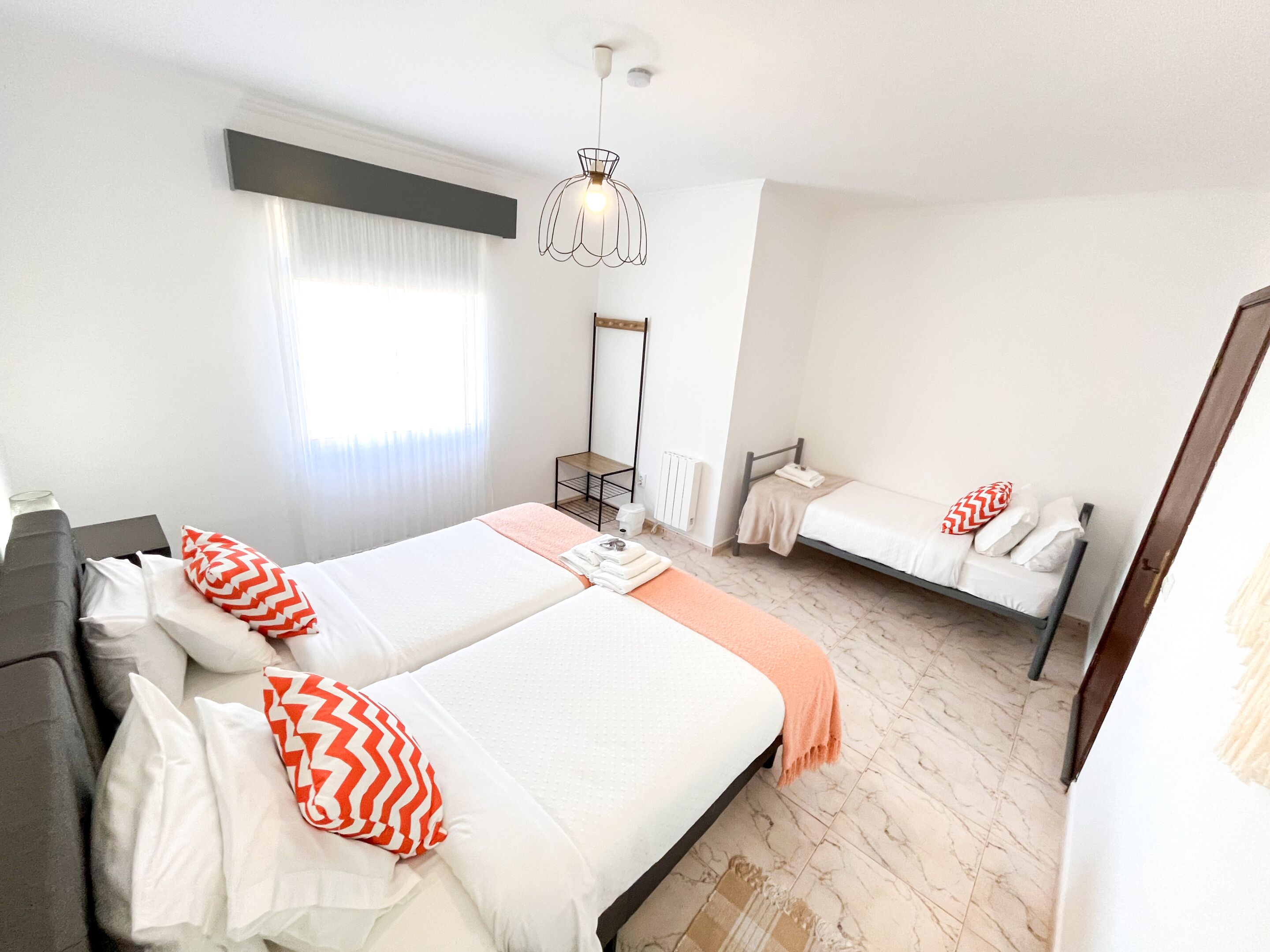 A modern hotel room with a large bed, a smaller bed, a desk, and a mirror.