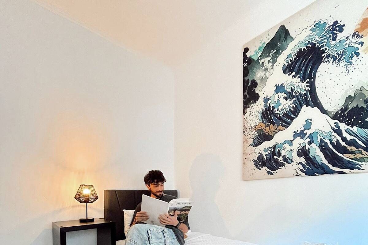 Ein Schlafzimmer mit einem Bett, einem Nachttisch, einer Lampe, einer Decke und einem Bild an der Wand.