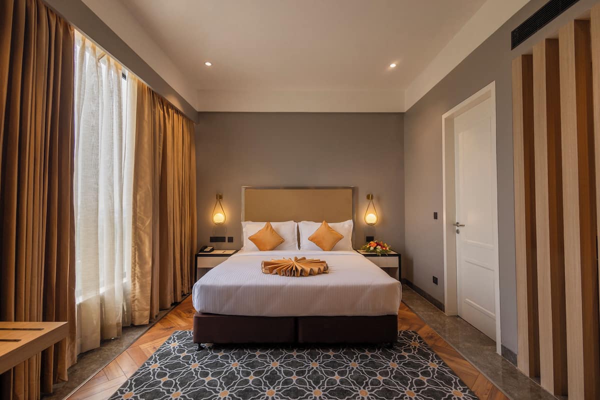 Ein Hotelzimmer mit einem großen Bett, zwei Nachttischen, einer Holzbank und einem gemusterten Teppich.