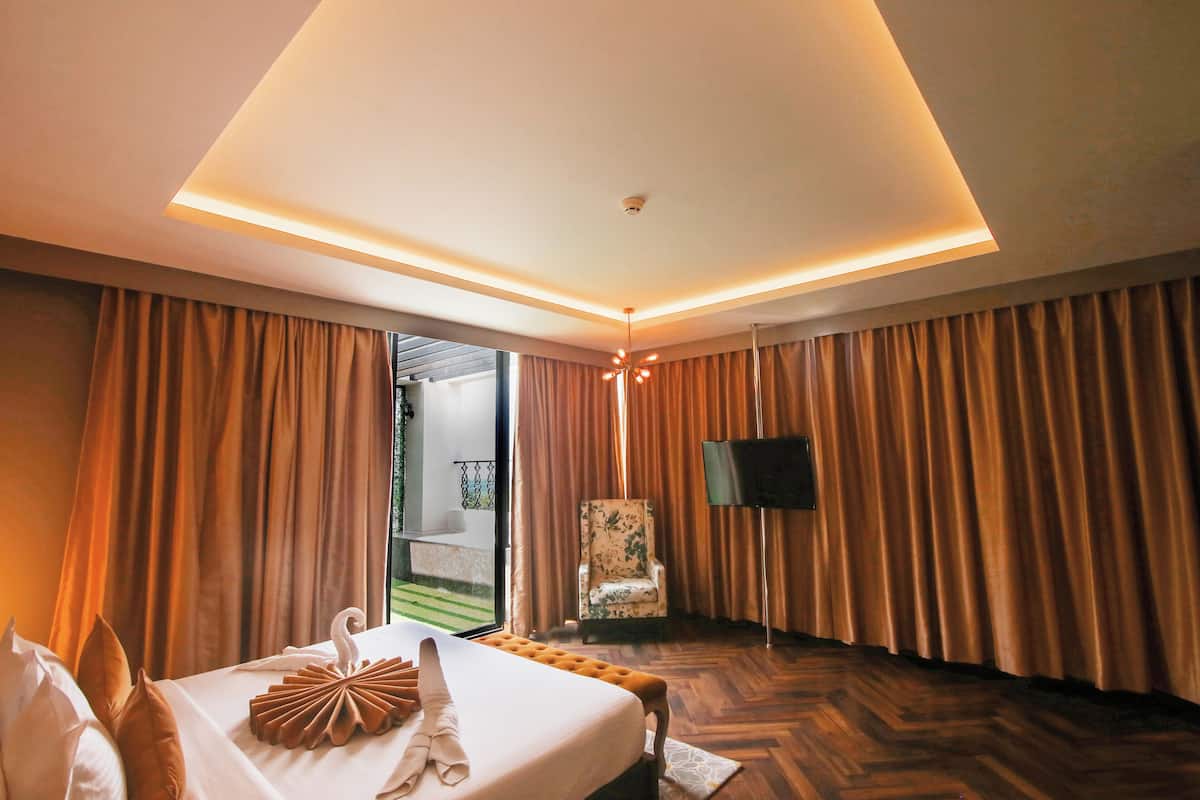 Ein Hotelzimmer mit Bett, Vorhängen, einem Sessel, einem Flachbildfernseher und einer Deckenleuchte.