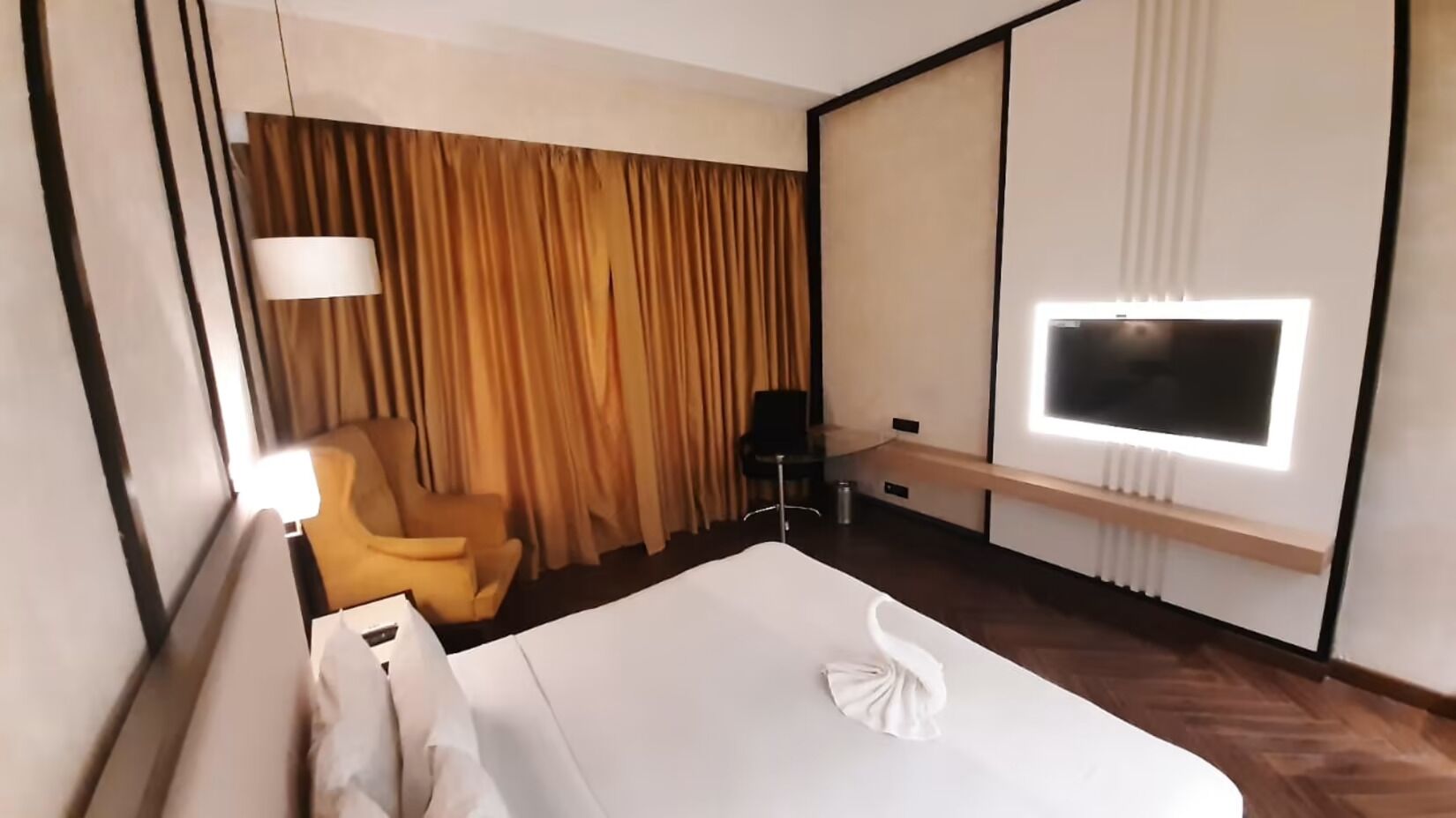 A hotel room with a large bed, a chair, a TV, and a curtain.