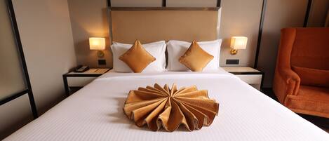 Una habitación de hotel con una cama bien hecha, dos lámparas de noche, un teléfono y un sillón naranja suave.