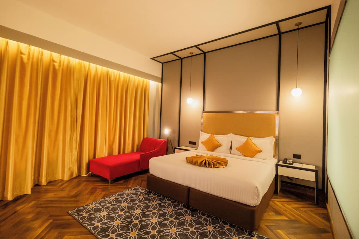 Ein Hotelzimmer mit einem großen Bett, einem roten Sessel, einem Nachttisch und einem gemusterten Teppich.