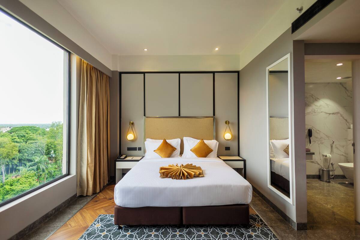Ein modernes Hotelzimmer mit einem großen Bett, Blick auf Grünflächen und einem Badezimmer mit Marmorwand.