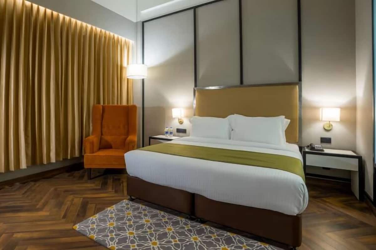 Ein Hotelzimmer mit Bett, Sessel, Nachttisch und einer Wand mit vertikalen Jalousien.