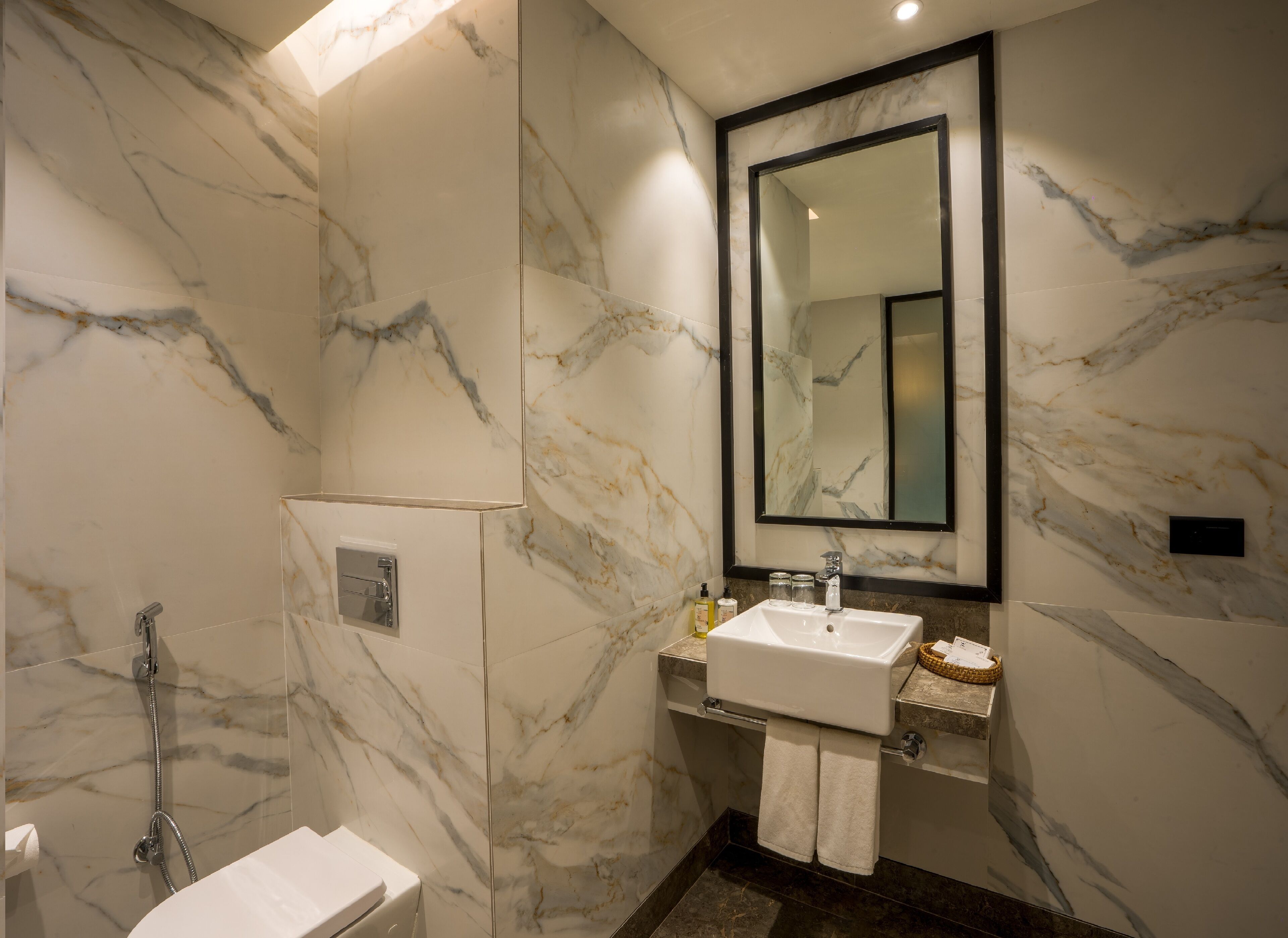 A bathroom with a marble wall, a large mirror, a sink, and a shower.