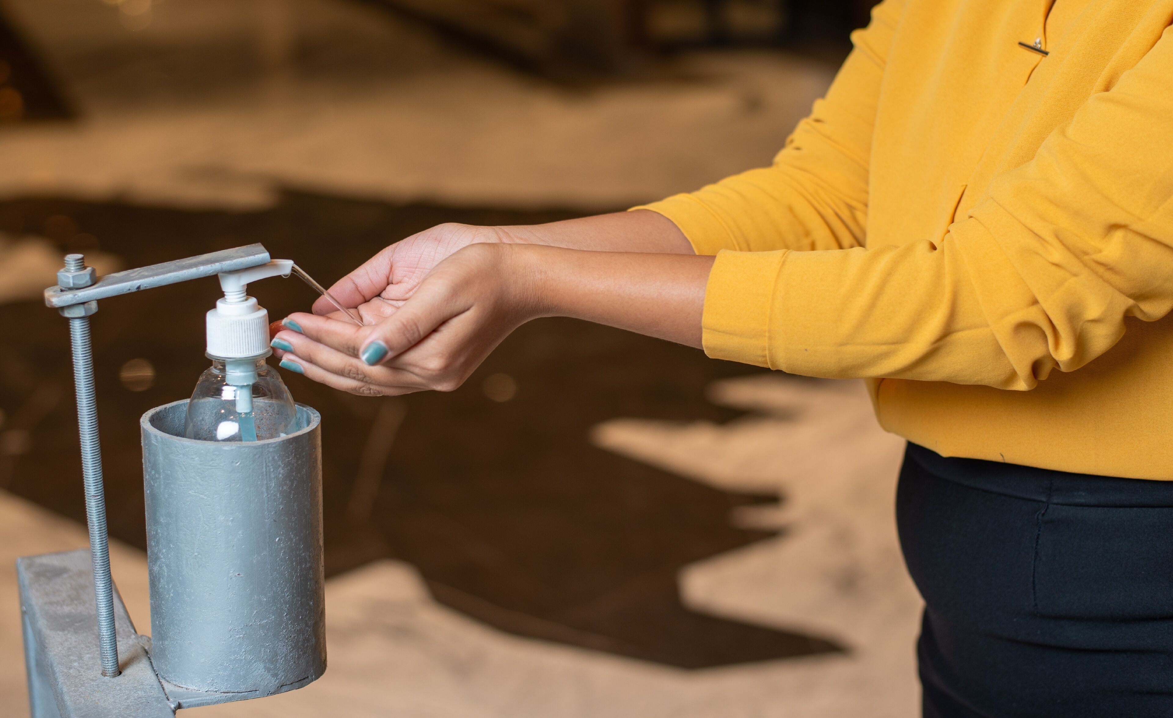 A person using a hand sanitizer dispenser mounted on a metal stand.