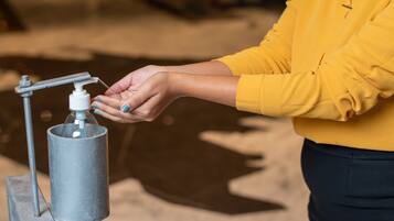 A person using a hand sanitizer dispenser mounted on a metal stand.