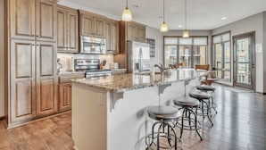 Une cuisine spacieuse avec des meubles en bois, un grand îlot central doté de tabourets, des appareils électroménagers en acier inoxydable et un éclairage suspendu.