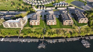 Vue aérienne d’un quartier résidentiel comprenant plusieurs immeubles d’appartements, une marina où sont amarrés des bateaux et un espace vert bien entretenu.