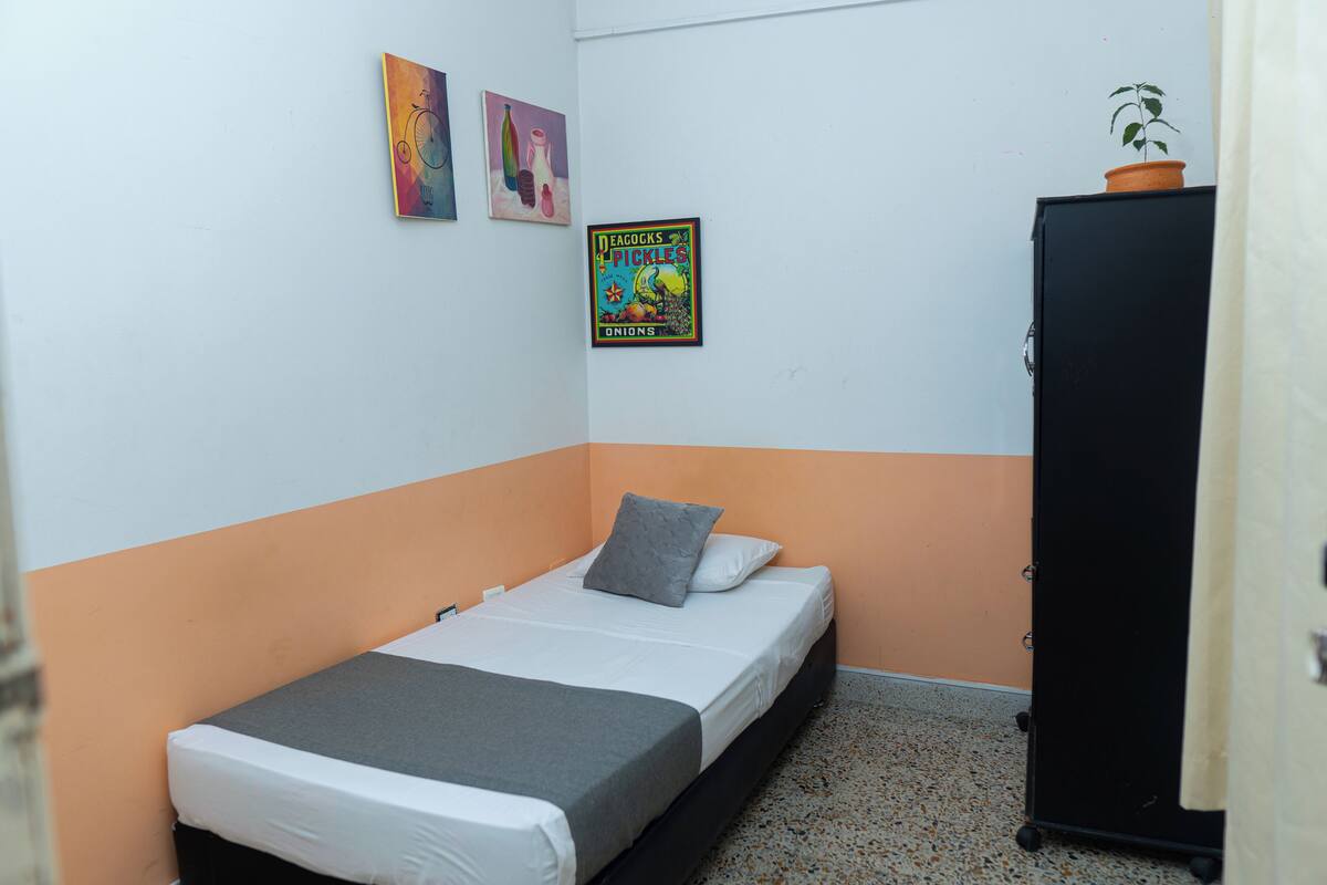 A small, single-bed room with a white and orange color scheme, a black wardrobe, and two wall art pieces.