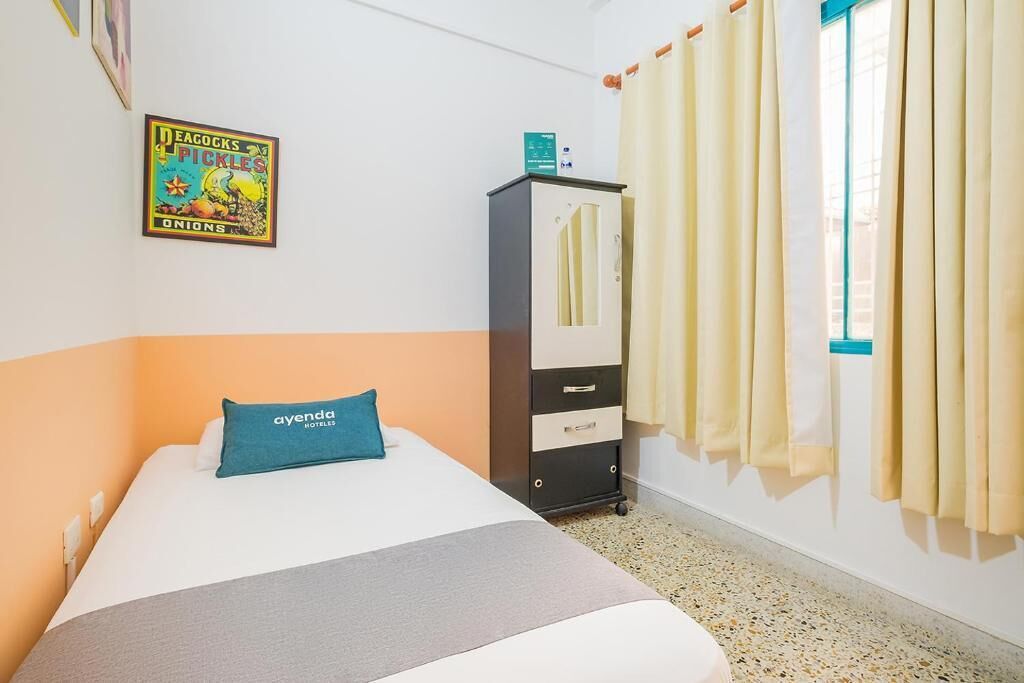 Une chambre d’hôtel avec un lit, un minibar, une fenêtre avec des rideaux et une affiche au mur.