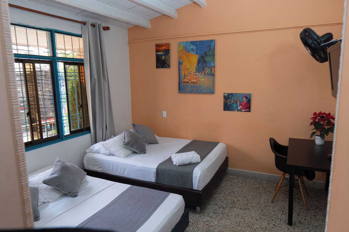 A hotel room with two beds, a desk, a chair, and artwork on the walls.