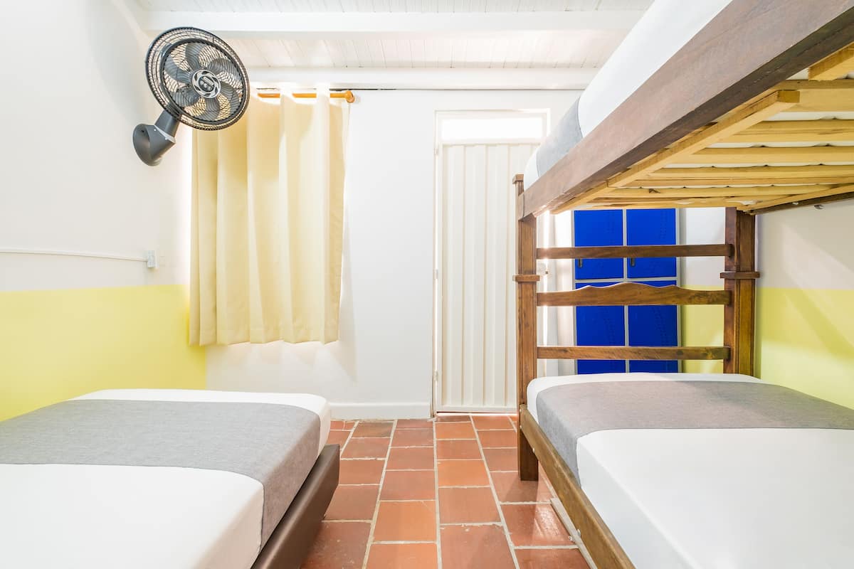 A room with two beds, a fan, a curtain, and a door.