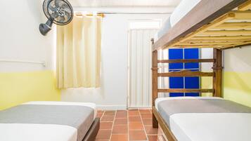 Una habitación con dos camas, un ventilador, una cortina y una puerta.