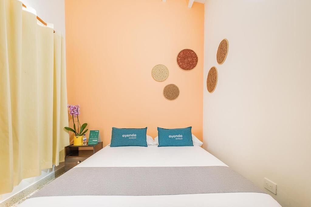 A hotel room with a bed, two pillows with the hotel name, a nightstand with a plant, and a wall with circular decorations.