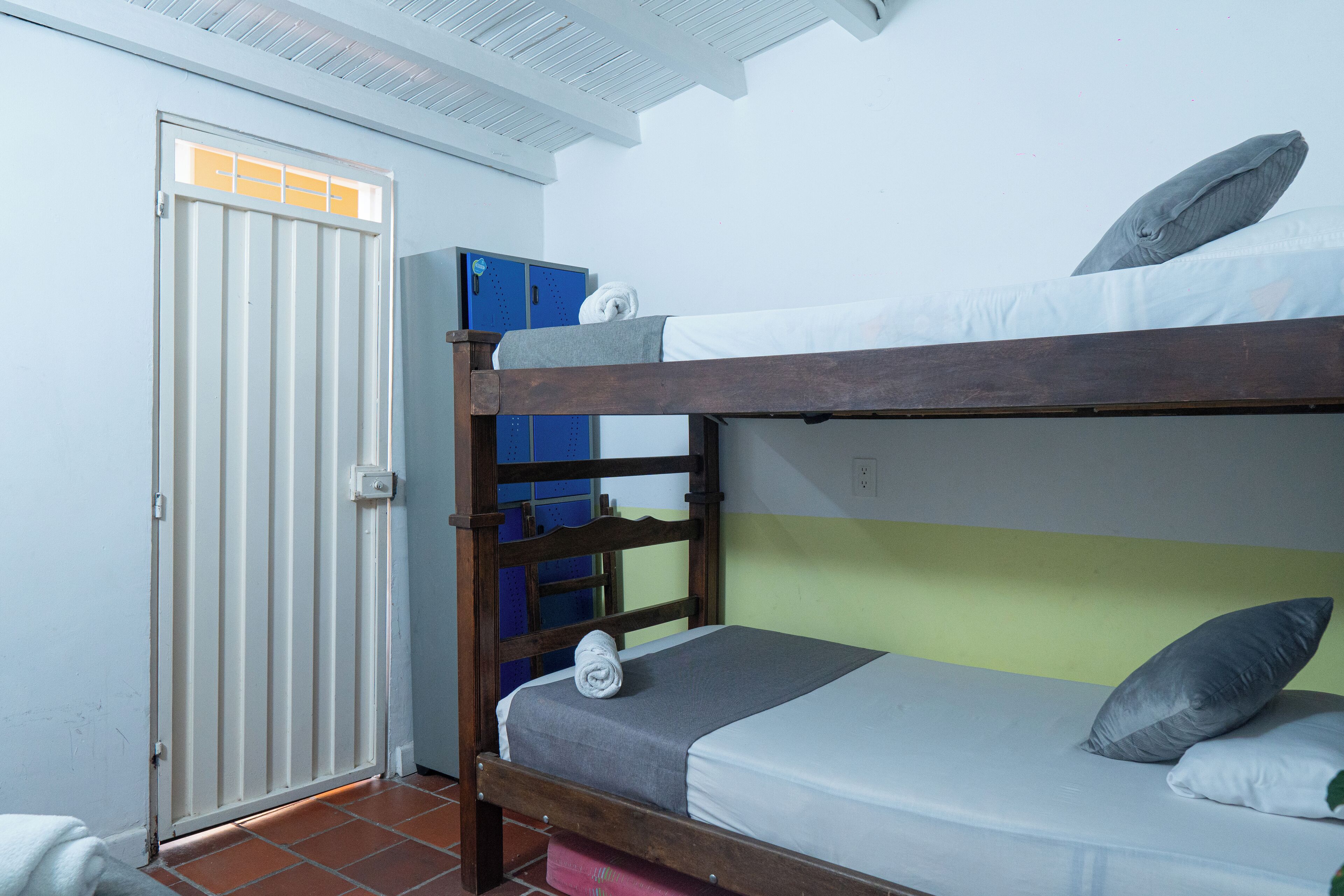 A bunk bed with a grey mattress and pillows, a wooden headboard, and a blue storage unit against the wall.